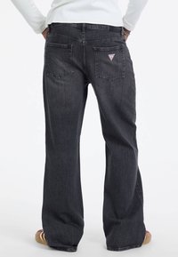 Ciemnoszare dżinsy z rozszerzanym krojem nogawek, dwoma tylnymi kieszeniami i małą trójkątną naszywką logo nad prawą kieszenią.