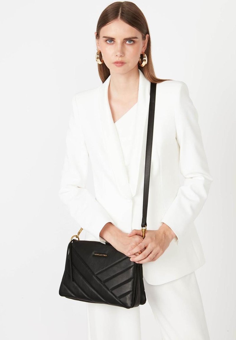 Sac en cuir noir à bandoulière avec motif matelassé, accents en métal doré et bandoulière ajustable. Forme rectangulaire, texture lisse.