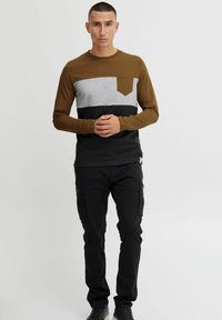 Majica dugih rukava s smešnim, sivim i crnim blokovima boja, s džepom na prsima. Materijal je mekan s prilagođenim dizajnom.