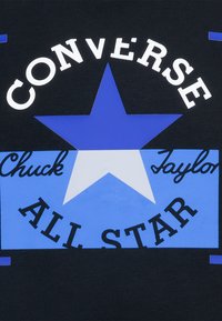 Tessuto nero con una grafica di una stella blu, accompagnato dal testo "Converse Chuck Taylor ALL STAR" visualizzato in caratteri bianchi e neri.