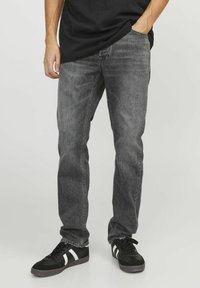 Vaqueros de mezclilla gris con corte recto, textura desgastada y diseño de cinco bolsillos. Combinados con zapatillas negras que tienen acentos blancos.