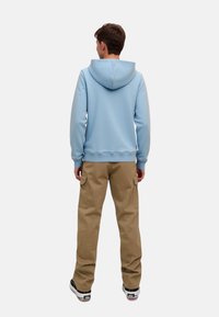 Svetlo modra kapuca z vrvico za zategovanje, v kombinaciji s khaki cargo hlačami. Kapuča ima gladko teksturo in oprijet manšete.