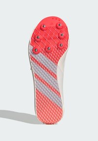 Semelle de chaussure de sport blanche avec un motif en caoutchouc rouge et gris, dotée de picots proéminents pour l'adhérence et d'une surface texturée pour une meilleure prise.