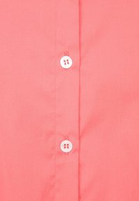 Camisa coral de botones, hecha de una tela suave, que cuenta con botones blancos y una tapeta ordenada. La textura es plana y uniforme.