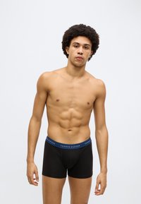 Mustad puuvillased bokserpüksid sinise vööga, millel on "TOMMY HILFIGER" logo. Disain on keha järgiv ja sileda tekstuuriga.