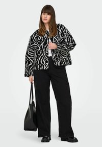 Juodai baltas zebra rašto švarkas su laisvu siluetu, priekinėmis kišenėmis ir apvalia iškirpte, derinamas su juodomis plačiomis kelnėmis ir juoda rankine.