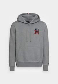 Szara bluza z kapturem wykonana z miękkiego materiału, z przednią kieszenią kangurzą oraz haftowanym logo w czerwonych i granatowych akcentach.