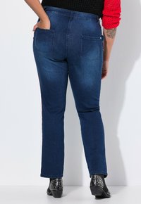 Tummansiniset farkut, joissa on suora lahkeen muotoilu, kaksi takataskua ja punaiset sivuakoristeet. Ne on yhdistetty mustiin nilkkureihin.