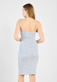 Kukallinen mekko, jossa on sinisiä kukkia valkoisella taustalla. Mekossa on ohuet olkaimet ja vartalonmyötäinen siluetti, joka loppuu polveen.
