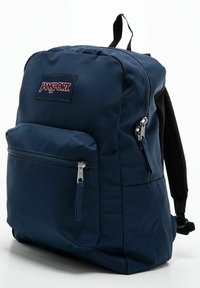 Niebieski plecak Jansport o prostokątnym kształcie, z przednią kieszenią na zamek, wyściełanymi czarnymi ramiączkami i teksturowanym materiałem.