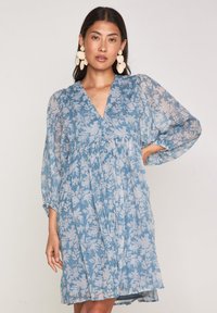 Abito floreale azzurro chiaro con scollatura a V, maniche lunghe trasparenti e corpino arricciato. Presenta una silhouette fluida e motivi floreali delicati.