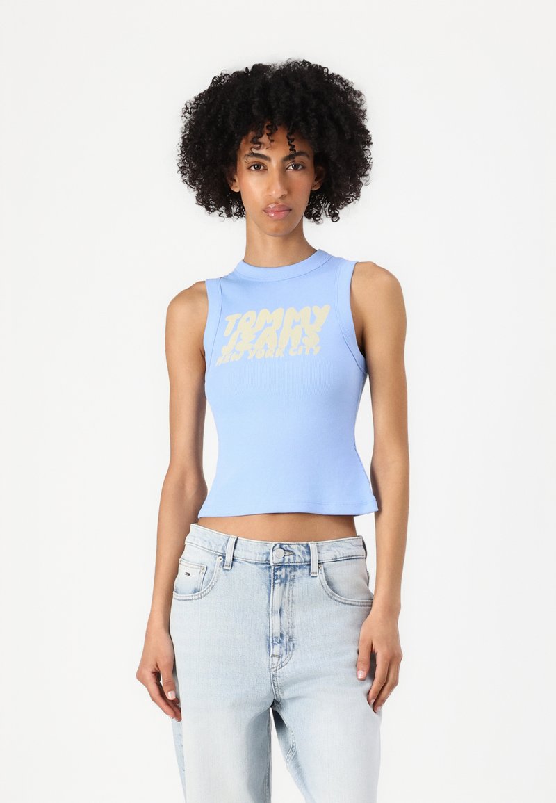 Top corto a costine blu con scollatura rotonda e grafica gialla "TOMMY JEANS NEW YORK CITY". Abbinate a jeans in denim chiaro, a silhouette aderente.