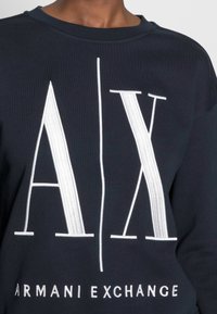 Mörk marinblå sweatshirt med en stor vit "A/X"-logotyp och texten "ARMANI EXCHANGE" längst ner, med en mjuk och len textur.