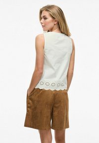 Hvit ermeløs topp med broderte utskjæringer på den nedre kanten, sammen med brune shorts i semsket skinnlignende materiale, med sidelommer.