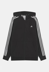 Haut à capuche noir zippé en tissu doux, avec une capuche, deux poches avant et trois rayures blanches le long des manches. Logo Adidas sur la poitrine.