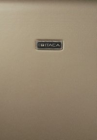 Bolsa de tela beige con un acabado texturizado. Cuenta con una placa rectangular de plata con el logo "ITACA" inscrito. Superficie lisa con acentos mínimos.