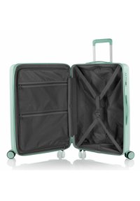 Valigia rigida di colore verde menta con chiusura a zip, interno grigio, più scomparti e cinghie incrociate per fissare gli oggetti.