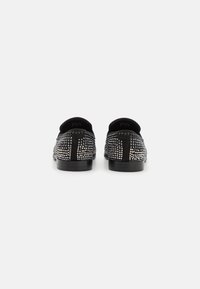 Chaussures noires avec une surface texturée, ornées de clous argentés disposés en motif géométrique, avec un bout arrondi et un talon bas.