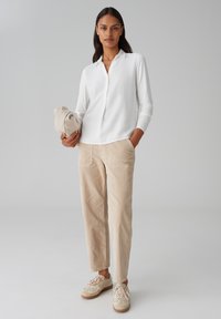 Witte lange mouwen kraagshirt, beige corduroy broek met voorzakken, en lichtgekleurde sneakers met gestructureerde veters.