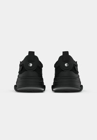 Chaussures de sport noires avec un dessus en mailles texturées, semelle rembourrée et une sangle à l'arrière, présentant des contours arrondis et un design élégant.
