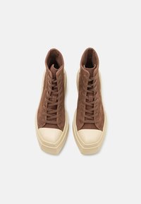 Sneakers înalte din suede maro cu șireturi, având o talpă din cauciuc crem și un vârf rotund. Finisaj texturat pe întreaga suprafață.