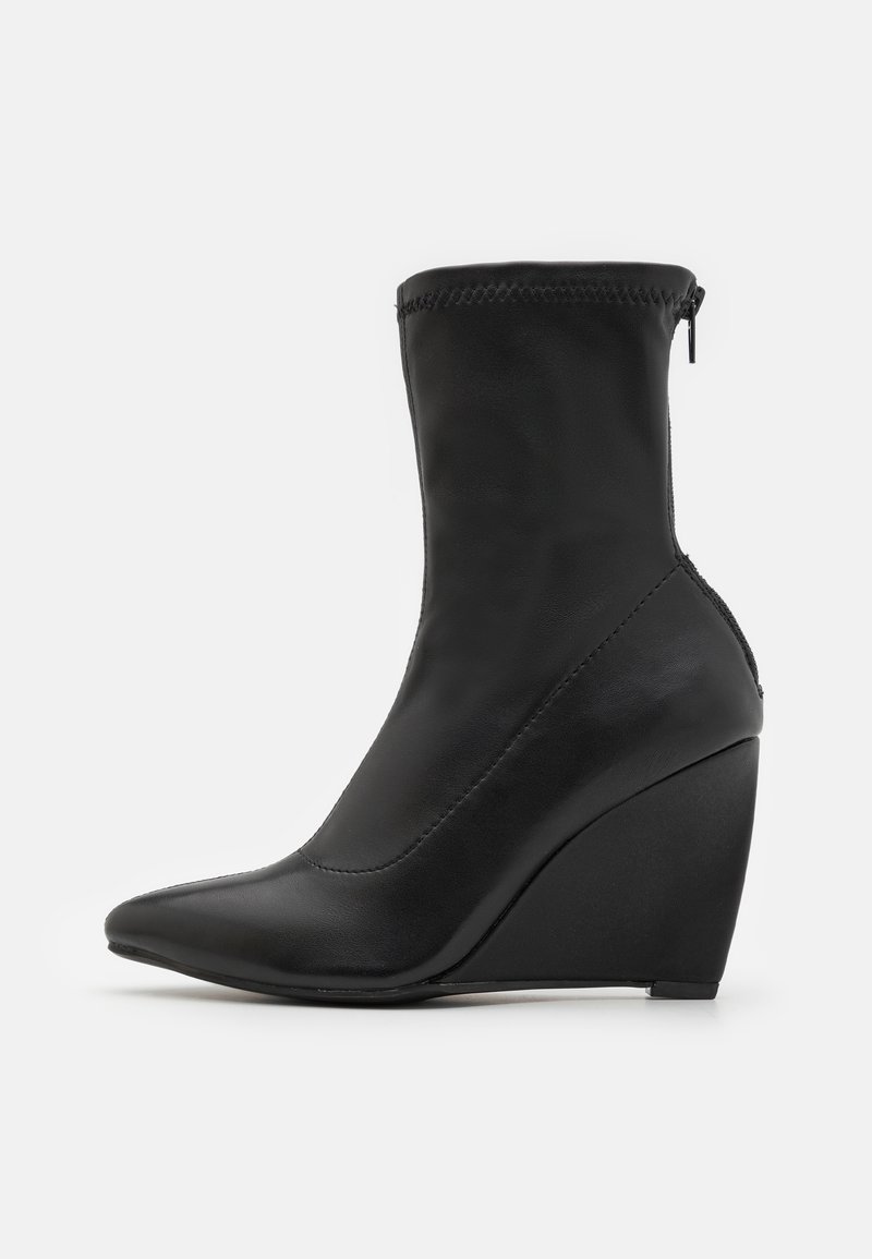 Bottine noire à cheville avec un bout pointu et un talon compensé. Fabriquée en cuir lisse, elle présente une fermeture éclair et un détail de surpiqûres.