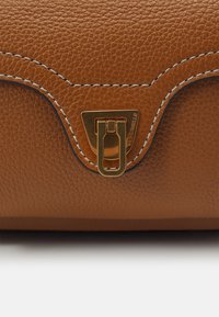 Ruskea teksturoitu nahkalaukku, jossa on kullanvärinen metallilukko. Laukussa on kaareva muotoilu ja kontrastina valkoinen ommel reunoilla.