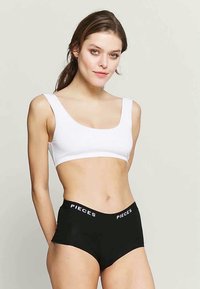 Fehér rövid topp széles pántokkal és négyzet alakú nyakkivágással. Fekete, magas derékú alsóruha "PIECES" logóval a rugalmas derékpánton.