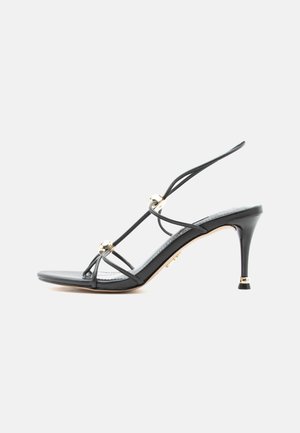 Sandale à talons hauts noire à fines lanières avec des accents de perles dorées sur un talon aigu à bout pointu.