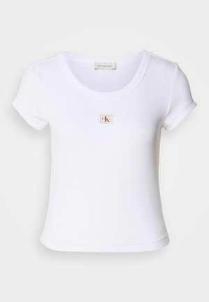 Camiseta ajustada blanca hecha de tela acanalada, con un cuello redondo y mangas cortas. Un pequeño logo de CK está bordado en el pecho.