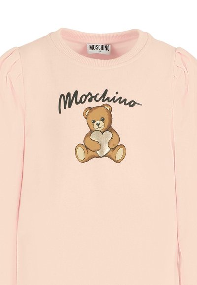 Różowa bluzka z długim rękawem i marszczonymi akcentami na ramionach, z nadrukiem misia trzymającego srebrne serce oraz napisem "Moschino" powyżej.