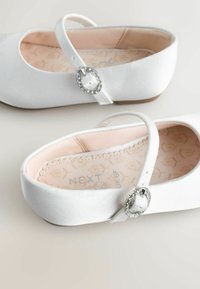 Scarpette da balletto in satin bianco con una sola cinghia alla caviglia decorata da una fibbia argentata e un interno rosa soft con un motivo floreale.