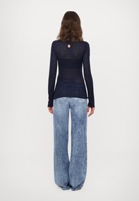 Maglia a maniche lunghe in maglia blu navy con dettaglio schiena scoperta, abbinata a jeans a gamba larga in denim chiaro con effetto sbiadito e tasche classiche.