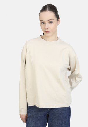 Beige langærmet sweatshirt med ribbet rundhals, afslappet pasform og detaljer i sidesømmen, båret over blå denimjeans.