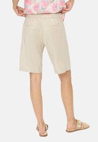 Shorts beige jusqu'aux genoux avec une taille élastique, deux poches arrière et un tissu lisse et léger. Associés à des sandales légères.