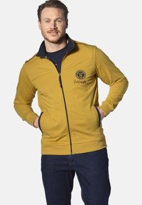 Gelbes Zip-Hoodie mit schwarzen Akzenten, gerippten Bündchen und einem runden Logo auf der Brust. Verfügt über Seitentaschen und einen hohen Kragen.