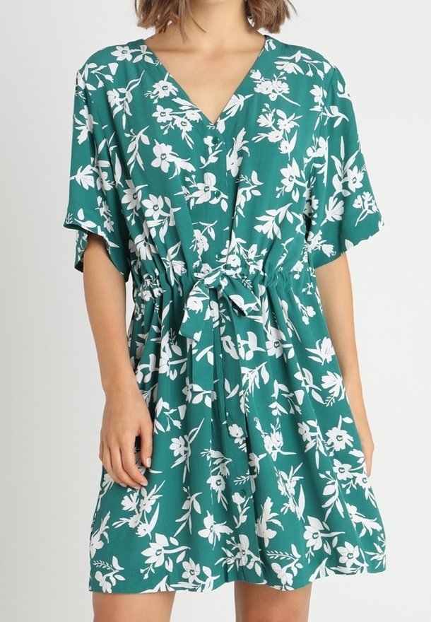 Robe bleu sarcelle avec un col en V, des manches courtes et une ceinture à nouer à la taille. Présente un motif floral blanc et une coupe décontractée. Texture de tissu douce.