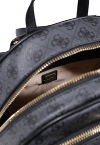 Zaino in finta pelle nera con motivo a rilievo, dotato di cerniere dorate, tre scomparti e un interno beige con dettagli del logo del marchio.