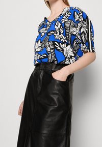 Blusa de manga corta en azul con un patrón floral en negro y blanco; combinada con una falda de cuero negra que presenta bolsillos laterales y una textura suave.