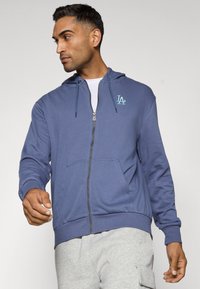 Mørkeblå zip-up hoodie med en kængurulomme, der har et lille lysblåt logo på brystet samt ribbede manchetter og kant.