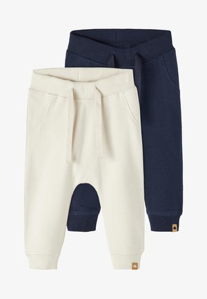 Two pairs of jogger pants, one cream and one navy, made of soft material with elastic waistbands, pockets, and ribbed cuffs.