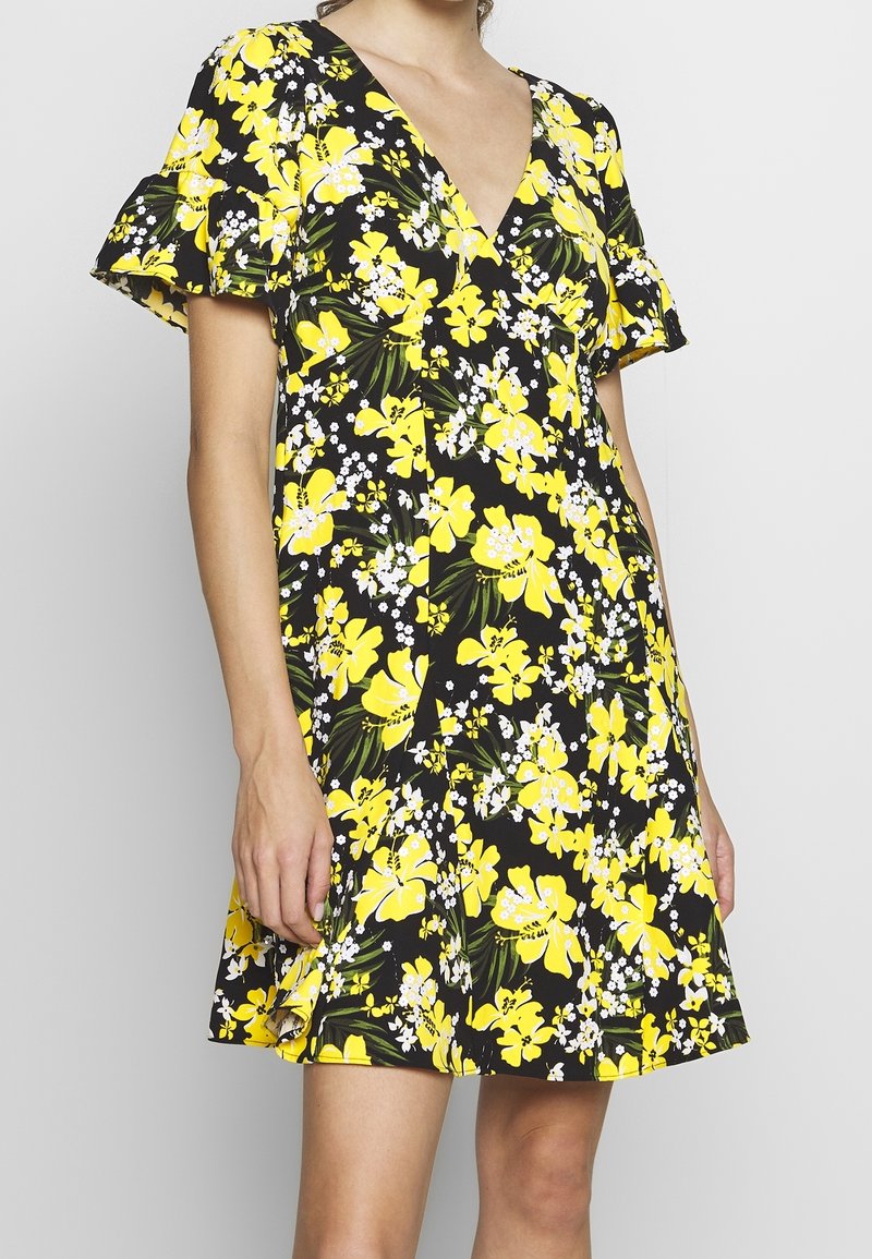 Vestido floral con fondo negro, adornado con flores amarillas y blancas. Escote en V, mangas cortas y suelto.