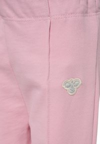 Roze stof met stikseldetails en een klein geborden wit en grijs bijenembleem aan de rechteronderzijde.