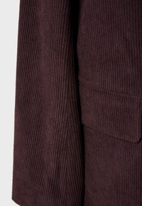 Tumma purppura neulospussin kangas, jossa on pystysuora ribbitekstuuri, näkyvä läppätasku ja helmapitsidetaljit.