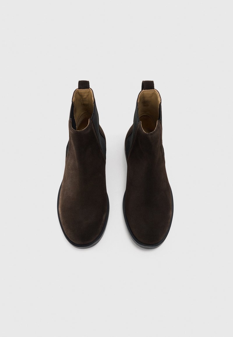 Braune Wildleder-Ankle Boots mit elastischen Seitenpanelen, glatter Oberfläche, runder Zehenform und Zugschlaufe hinten. Minimalistisches Design, flache Sohle.