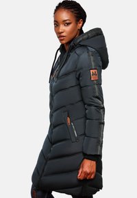Donkerblauwe pufferjas met capuchon, verticale gestreepte accenten, ritszakken en een logo patch op de mouw. Gelaagd materiaal.