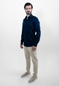 Marineblauw overhemd met lange mouwen, beige chino's en lichtgrijze instappers. Glad materiaal met een getailleerde pasvorm.