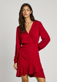 Robe enveloppante rouge avec manches longues, taille froncée et ourlet à volants. Tissu texturé et décolleté en V profond. Convient pour diverses occasions.