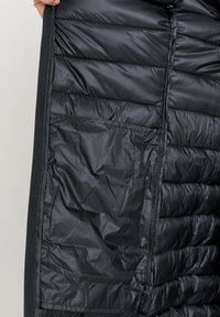 Zwarte pufferjack binnenkant toont gequiltte isolatie, soepele textuur en een zijzak. Bevat een volledige ritssluiting en gestikte details.