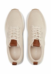 Sneakers beige in rete con superficie testurizzata, punta tonda e suola bianca. Accenti in pelle marrone sulla parte posteriore e sulla linguetta aggiungono dettagli.